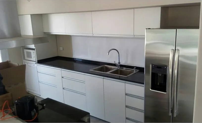 Cocina blanca a medida con cajones de cierre suave, tiradores continuos de aluminio y mesada negra, fabricada en nuestro taller de General Roca