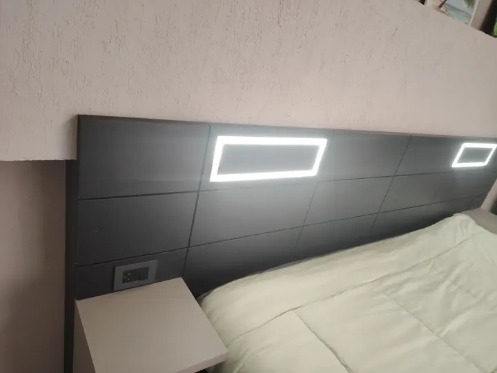 Detalle de respaldo de cama oscuro con marcos de luz LED encendidos y mesa de luz flotante, fabricado a medida en nuestro taller de General Roca