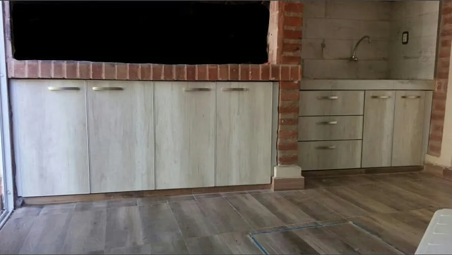 Bajo mesada largo con puertas en melamina Helsinki debajo de una parrilla de ladrillo y sector de bacha al costado, mueble para quincho fabricado en nuestro taller de General Roca